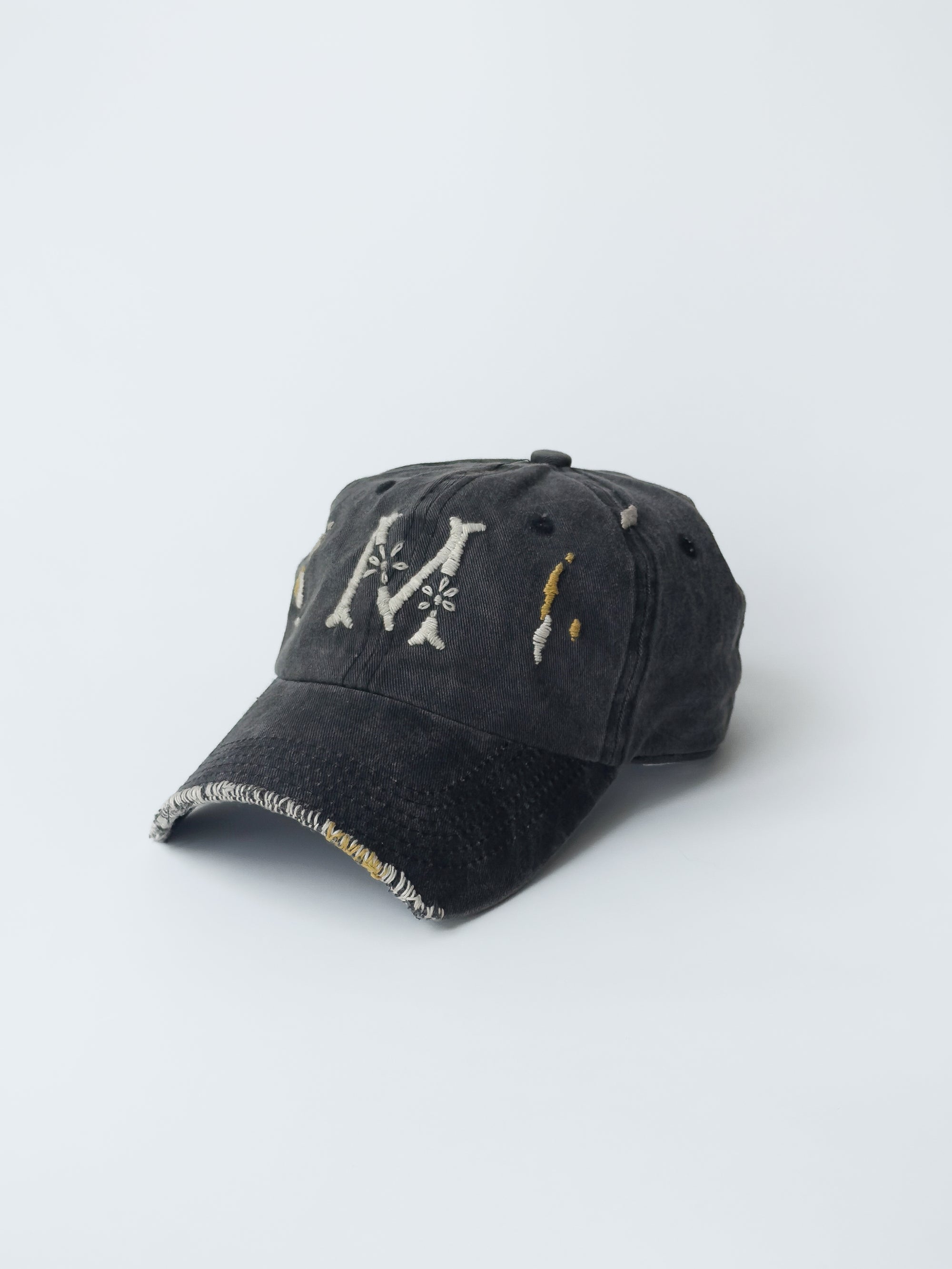 La casquette washed black d'objet, hand embroidered, frayed, side picture with M signature logo.