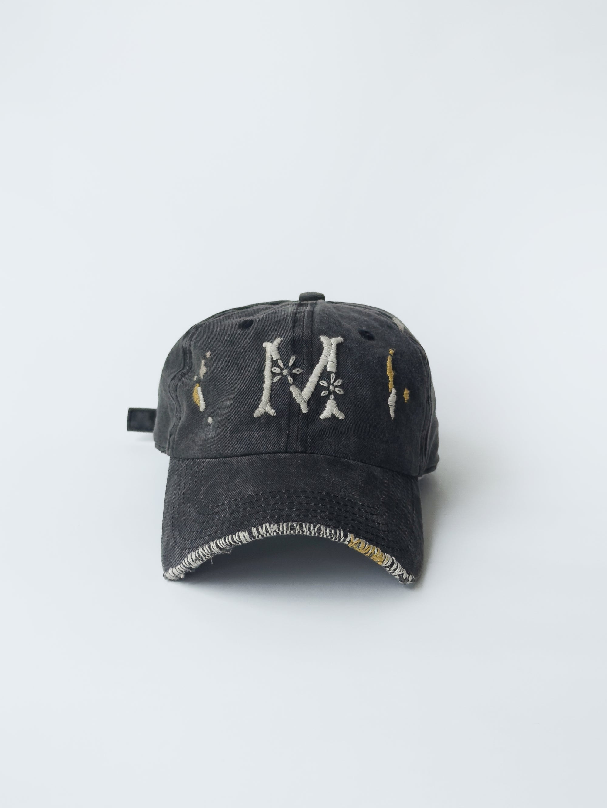 La casquette washed black d'objet, hand embroidered, frayed, front picture with M signature logo.