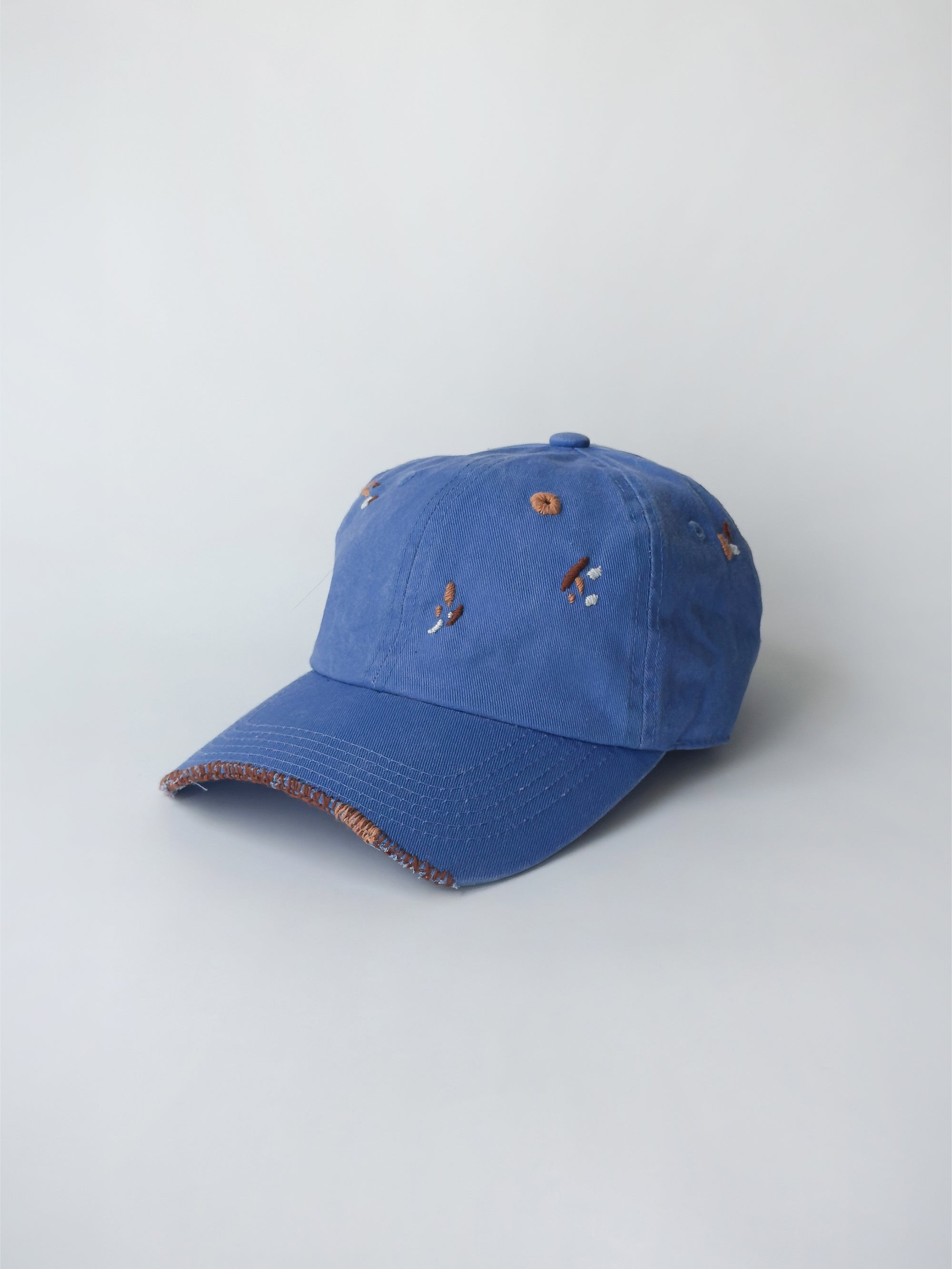 La casquette washed blue d'objet, hand embroidered, frayed, side picture, with brown and orange thread.
