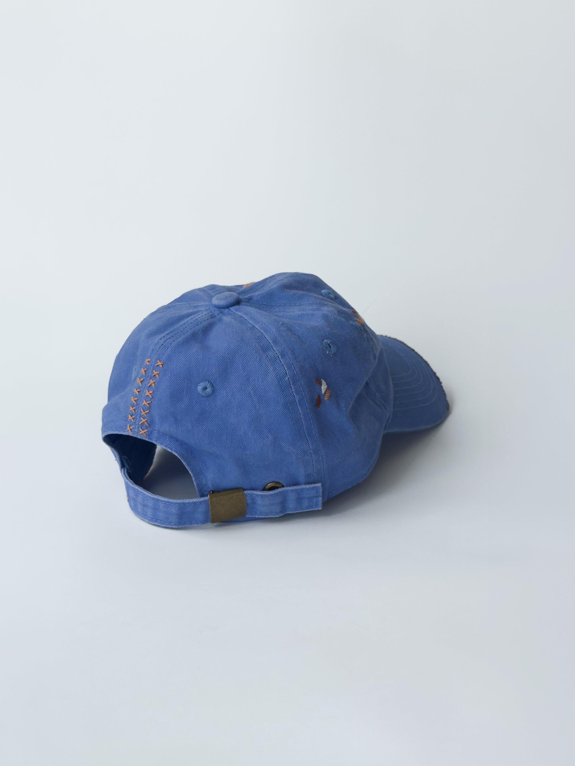 La casquette washed blue d'objet, hand embroidered, frayed, 3/4 back picture, with brown and orange thread.
