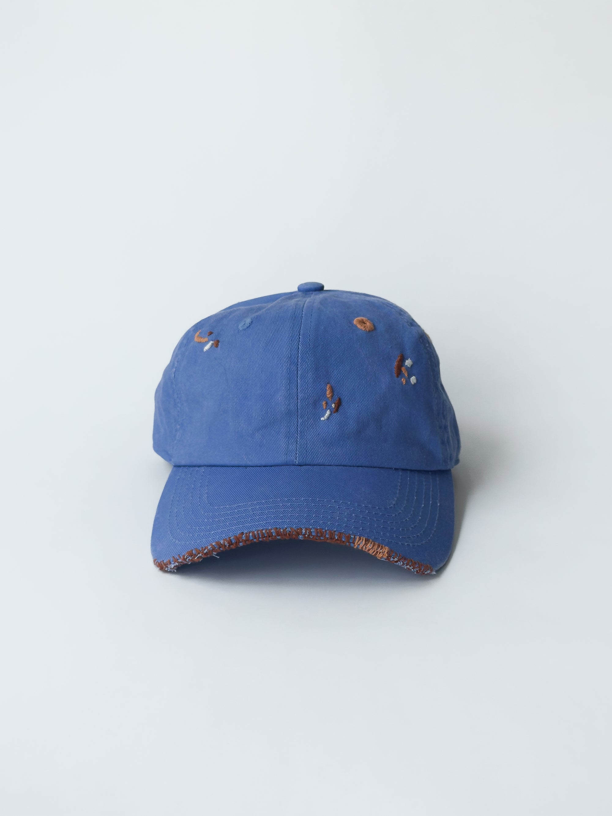 La casquette washed blue d'objet, hand embroidered, frayed, front picture, with brown and orange thread.